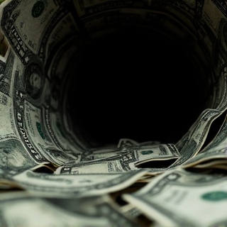 A dark, moody close-up of scattered dollar bills being pulled into a black hole or vortex, with dramatic lighting creating shadows that suggest money disappearing into an abyss.